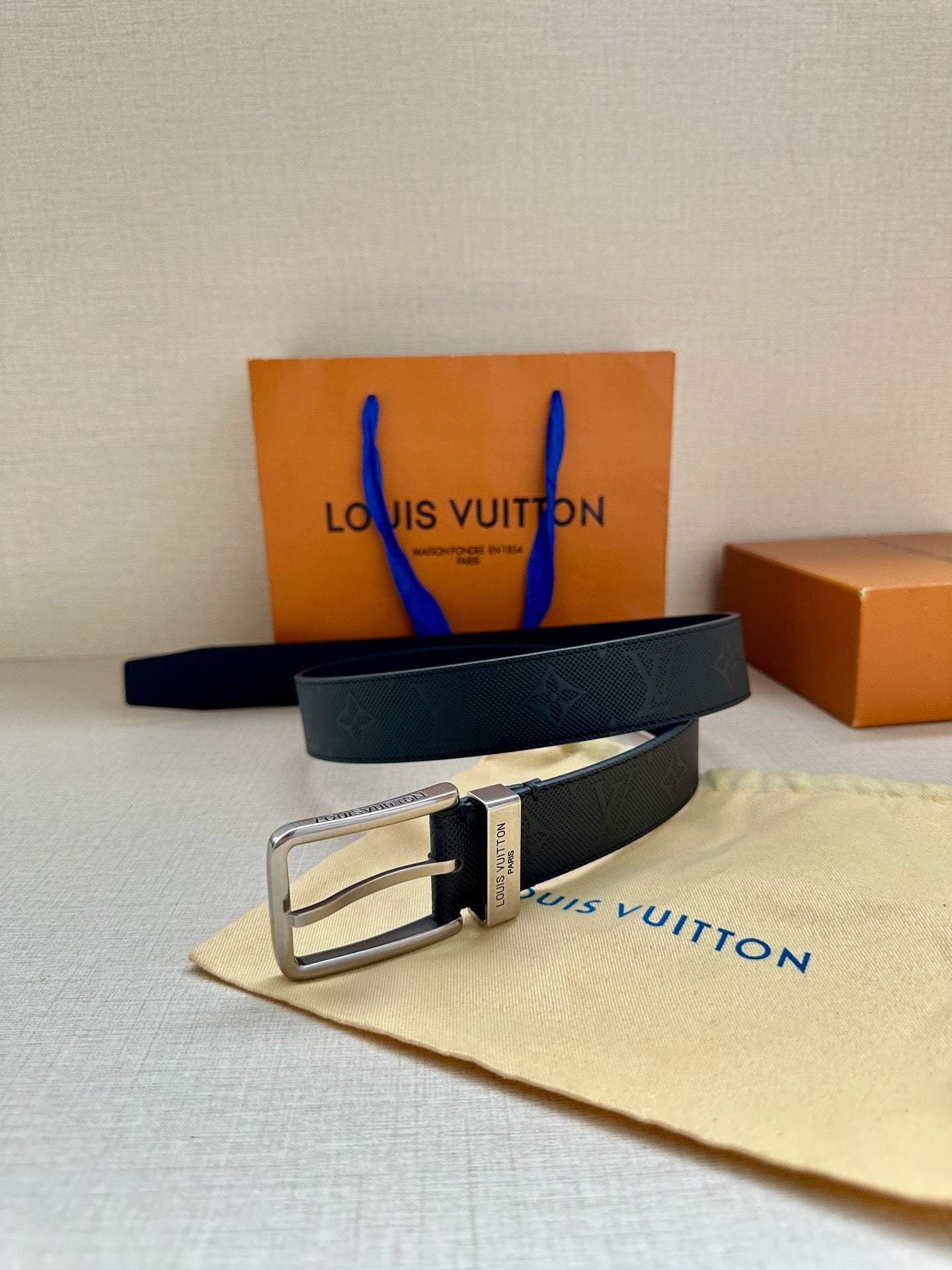Louis Vuitton belt with silver buckle and dark navy embossed strap, laid on pouch.