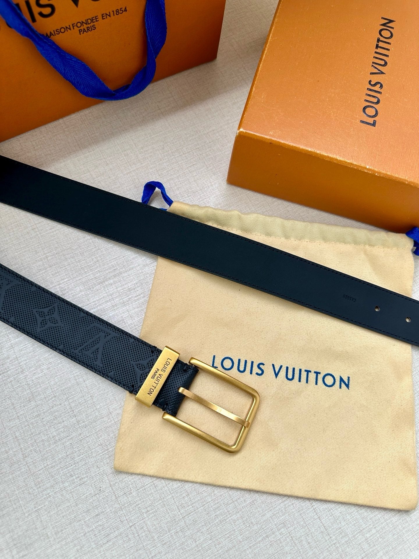 Louis Vuitton belt with gold-tone buckle and dark navy embossed strap on cream pouch.