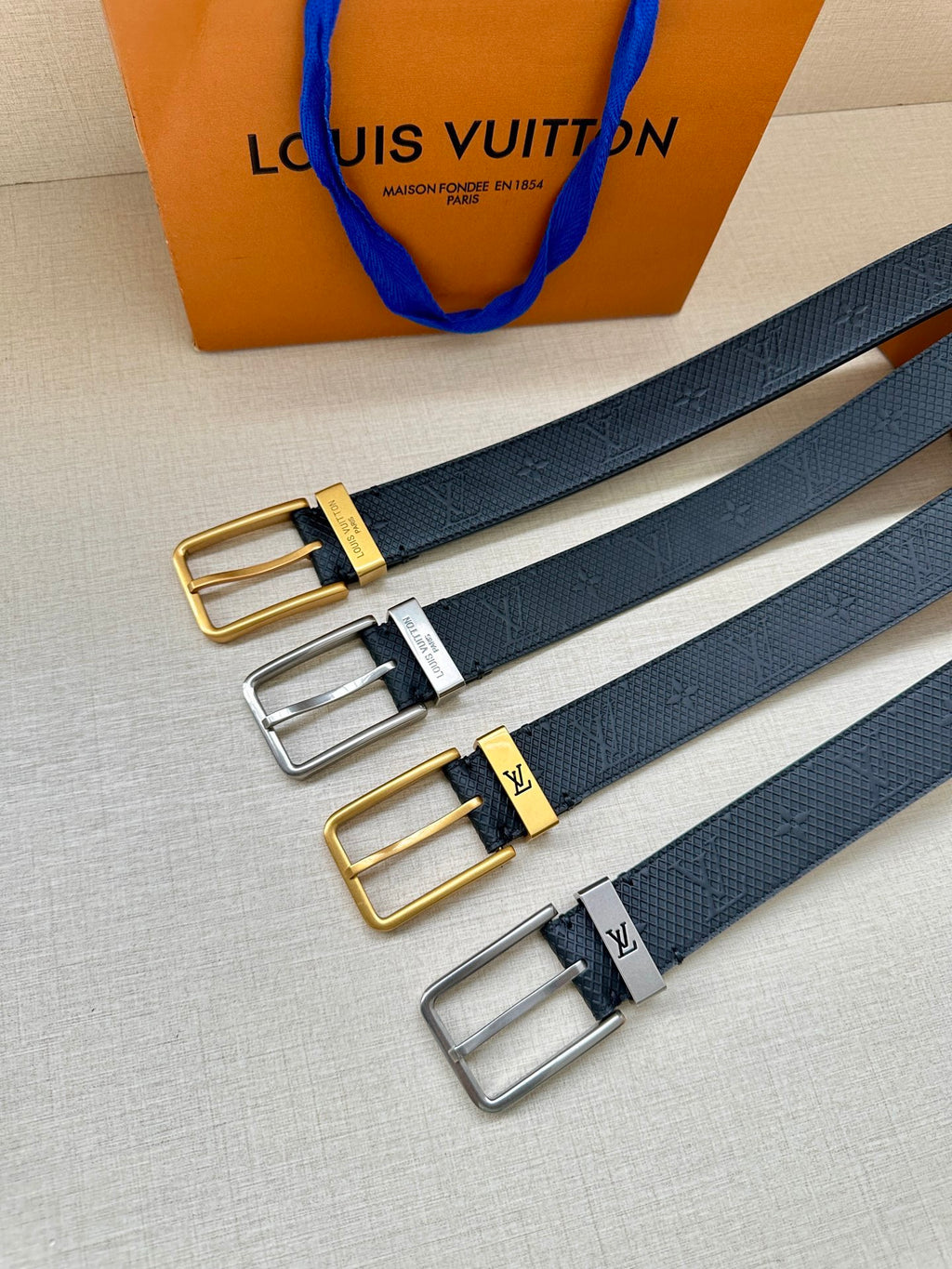 Louis Vuitton belt set with gold, silver, and black buckles on navy embossed straps.