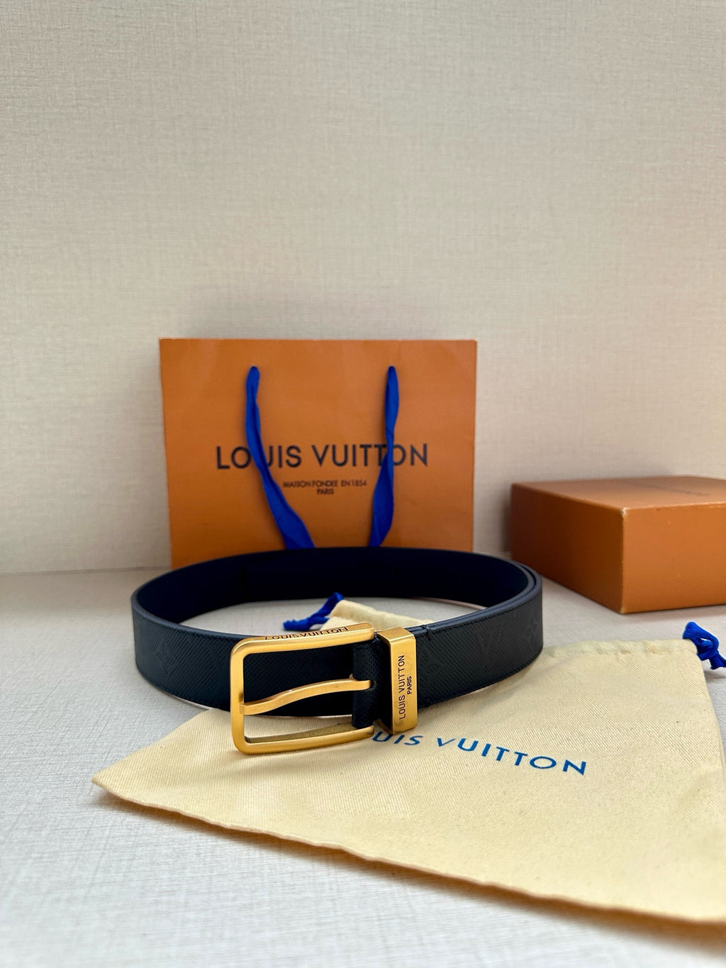 Louis Vuitton belt on cream pouch with dark navy embossed strap and gold-tone buckle.