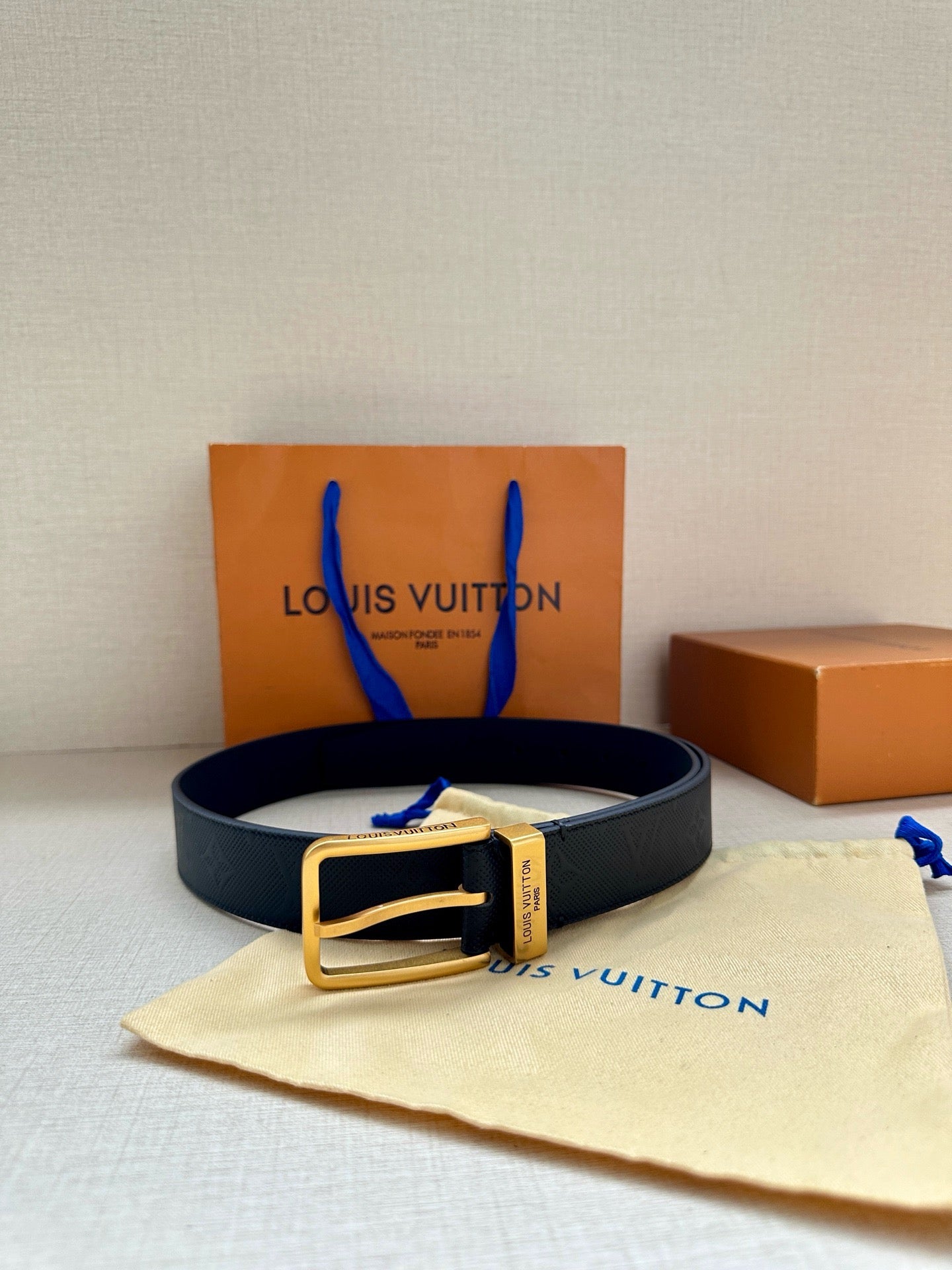 Louis Vuitton belt on cream pouch with dark navy embossed strap and gold-tone buckle.
