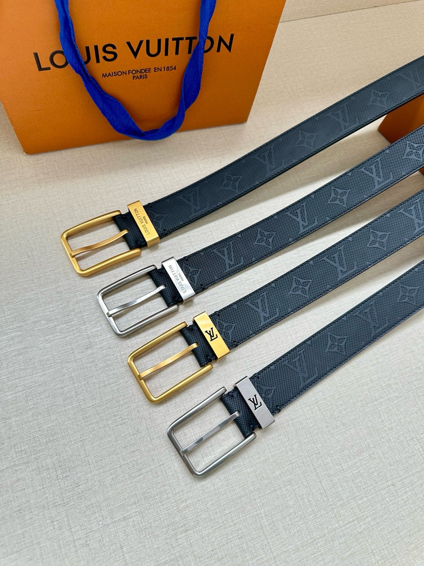 Louis Vuitton belt set with three buckle finishes—gold, silver, and black—on navy straps.