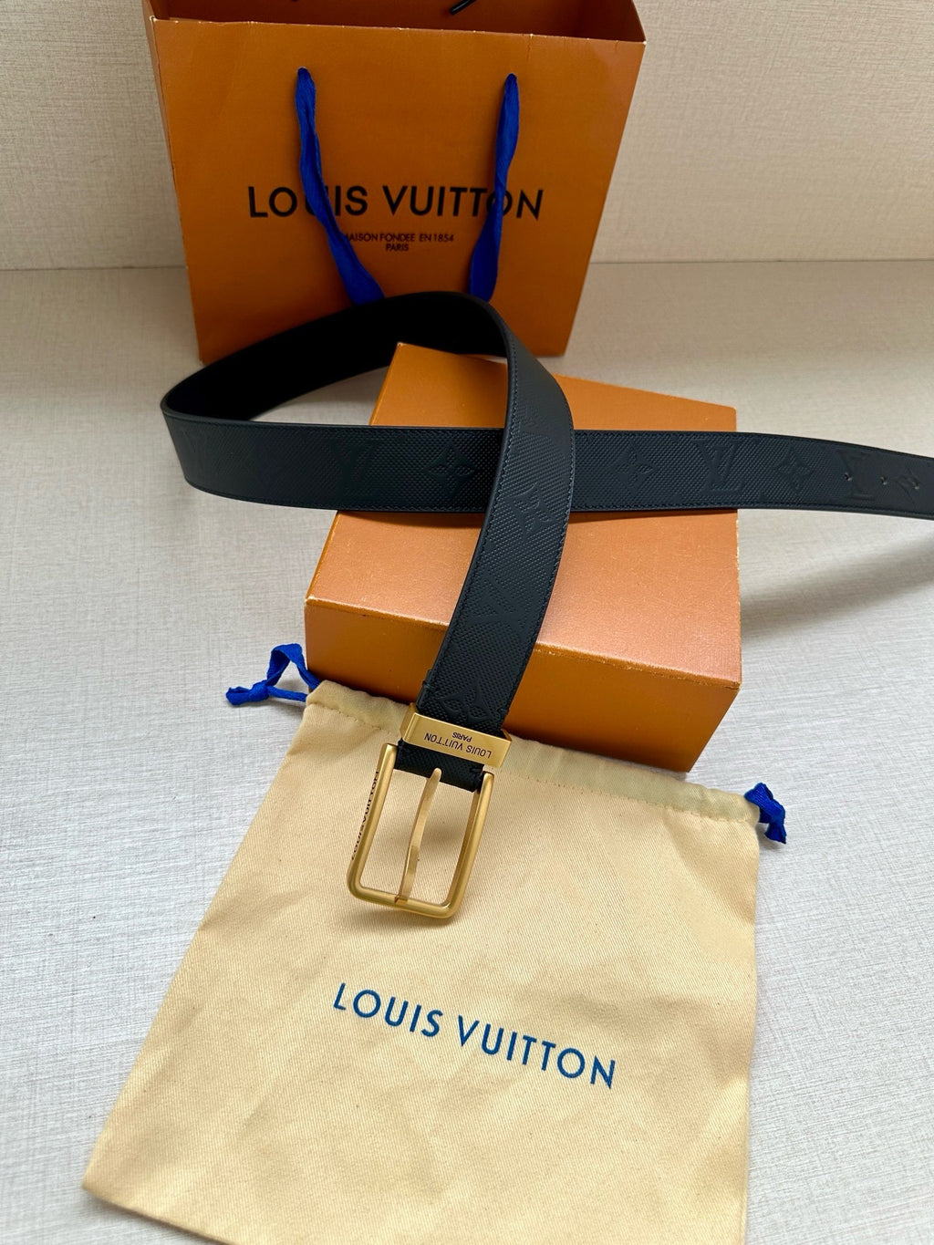 Louis Vuitton belt with gold-tone buckle on dark navy embossed strap, styled with pouch.