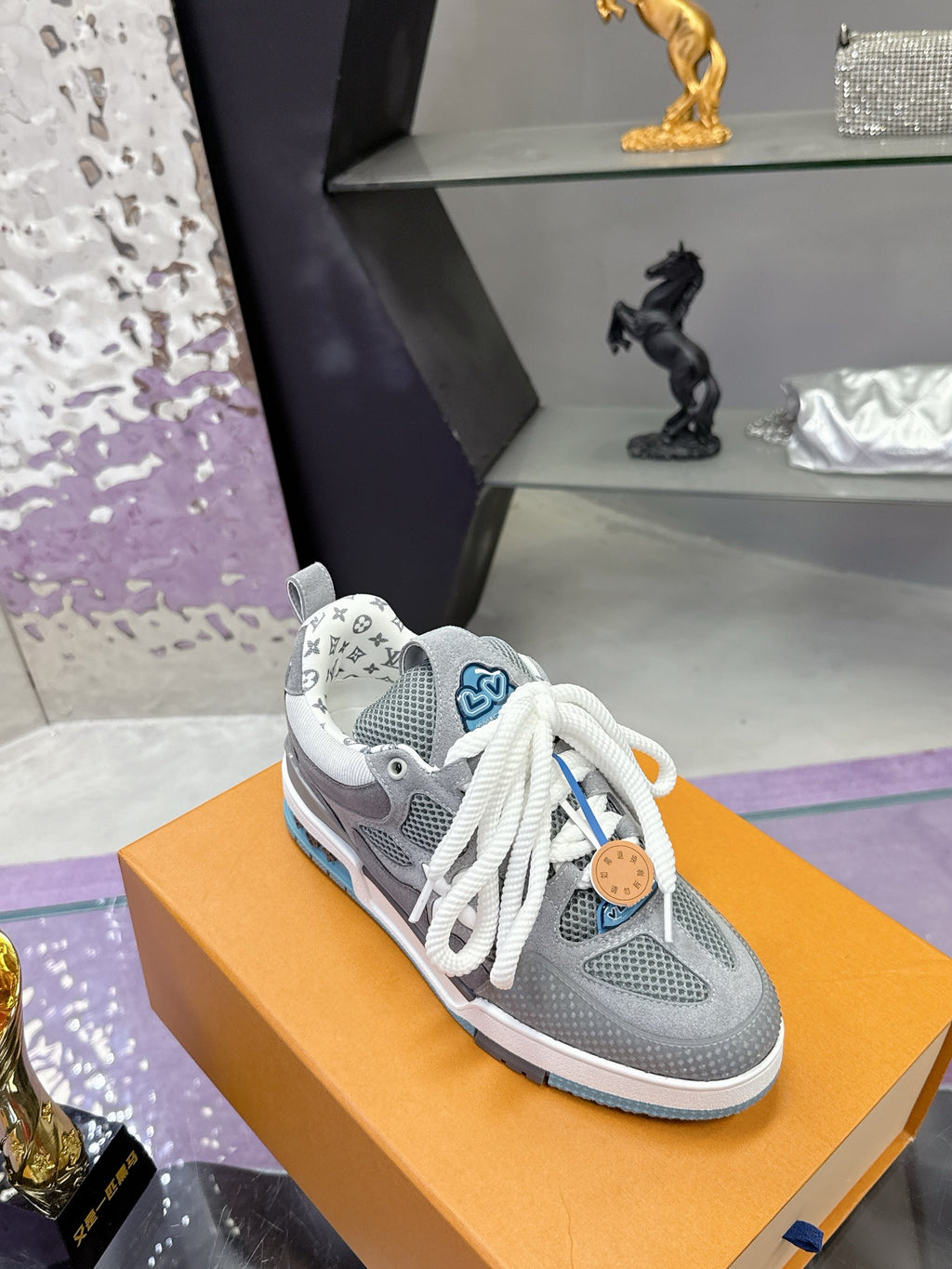 Gray low-top sneakers with white laces, LV-pattern heel patch, and blue outsole