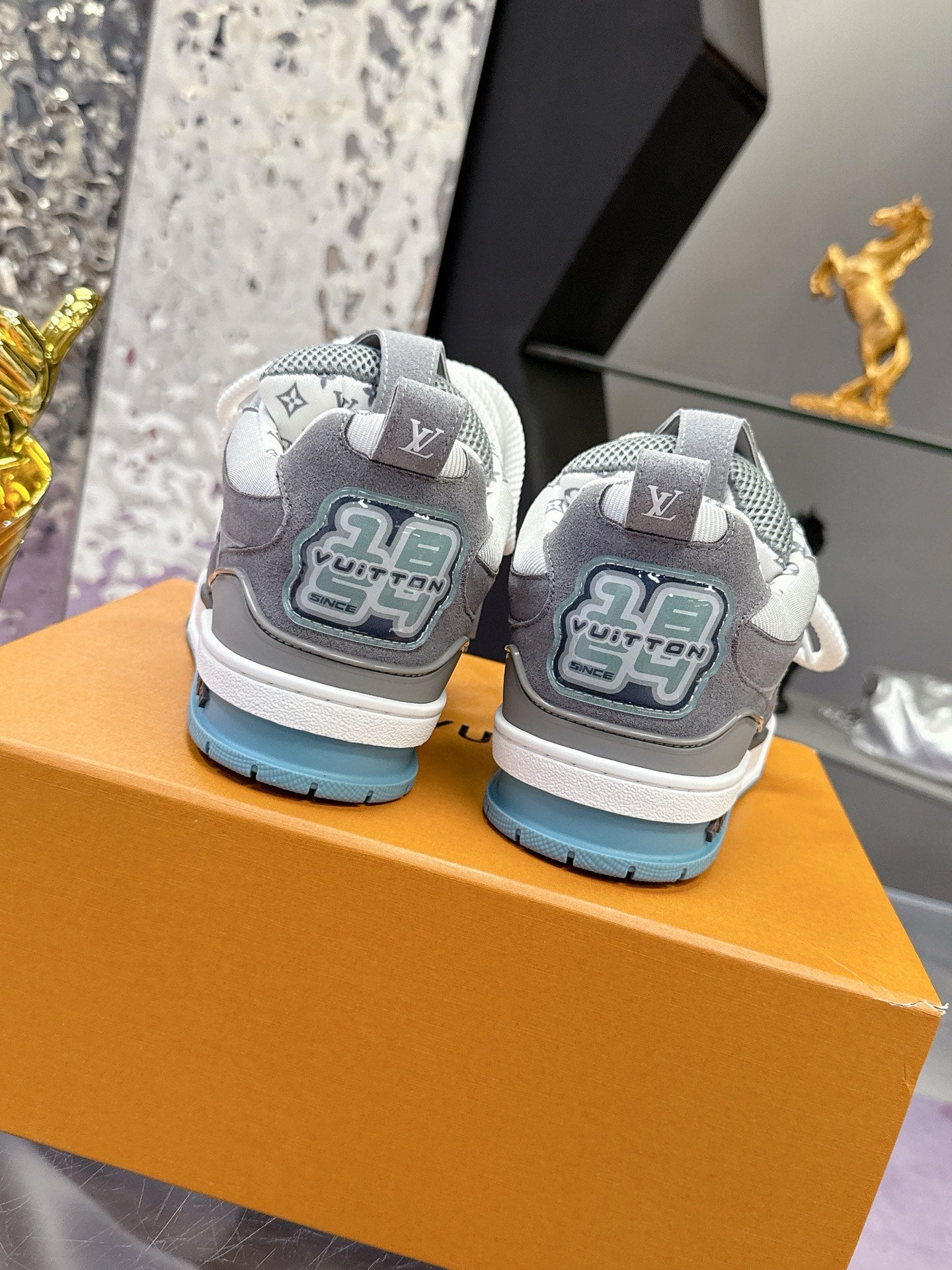 Rear view gray sneakers with white laces, LV logo on heels, and blue outsole