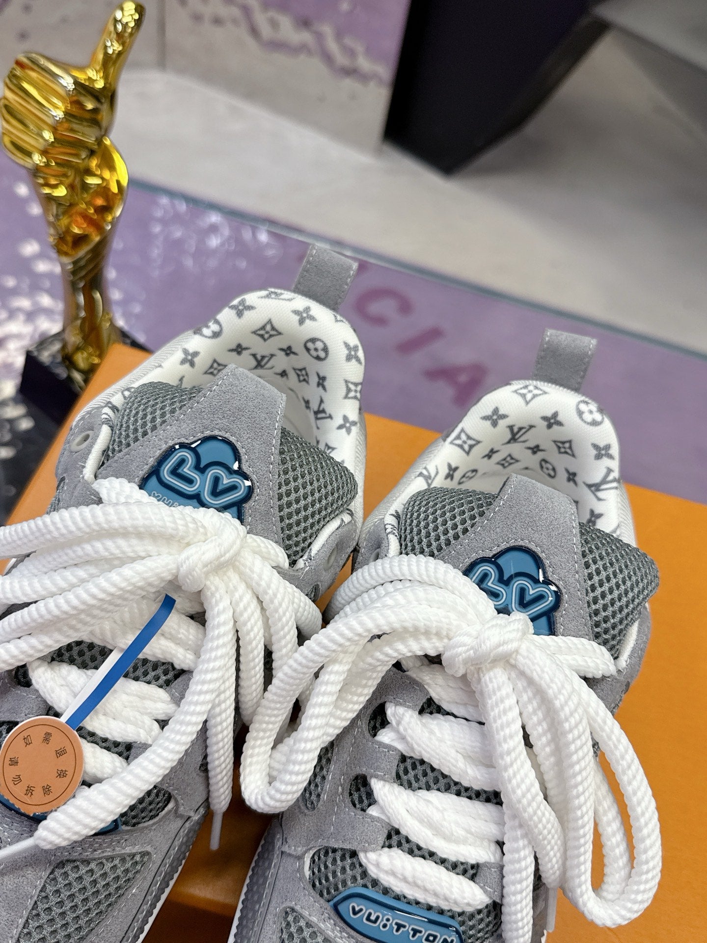 Close-up of gray sneakers with white laces, LV monogram heel, and blue logo