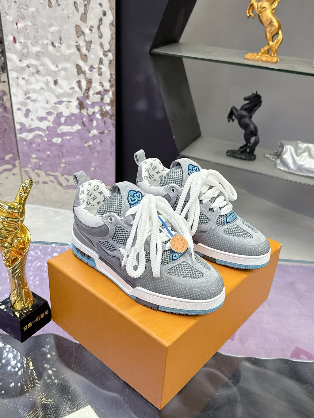 Gray low-top sneakers with white laces and blue side stripe, on orange box