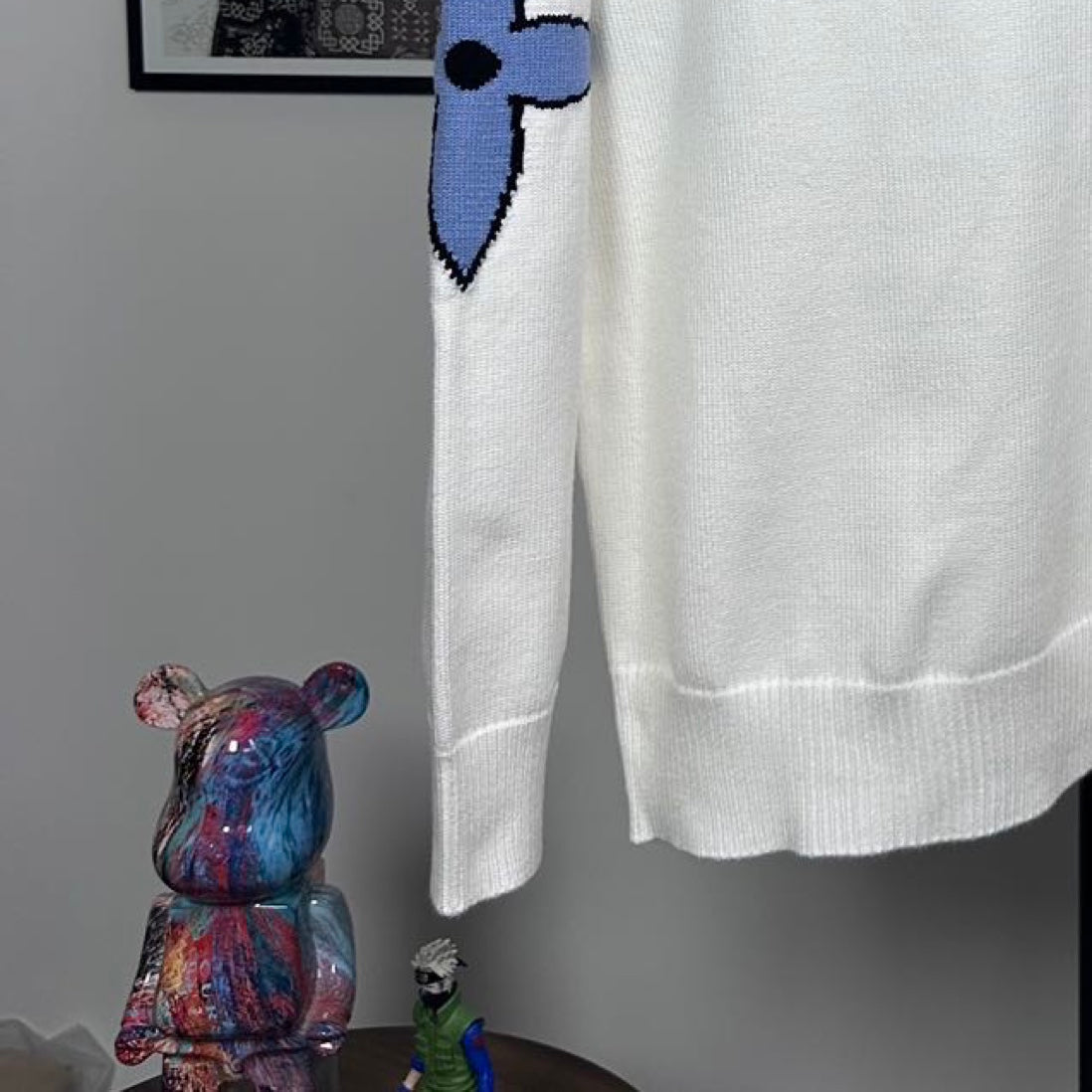 Long-sleeve knit sweater in white with blue bow-like logo detail and ribbed hem