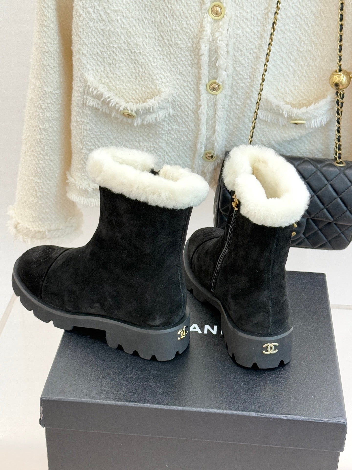 Black suede ankle boots with white shearling cuffs, chunky lug sole, on gray box