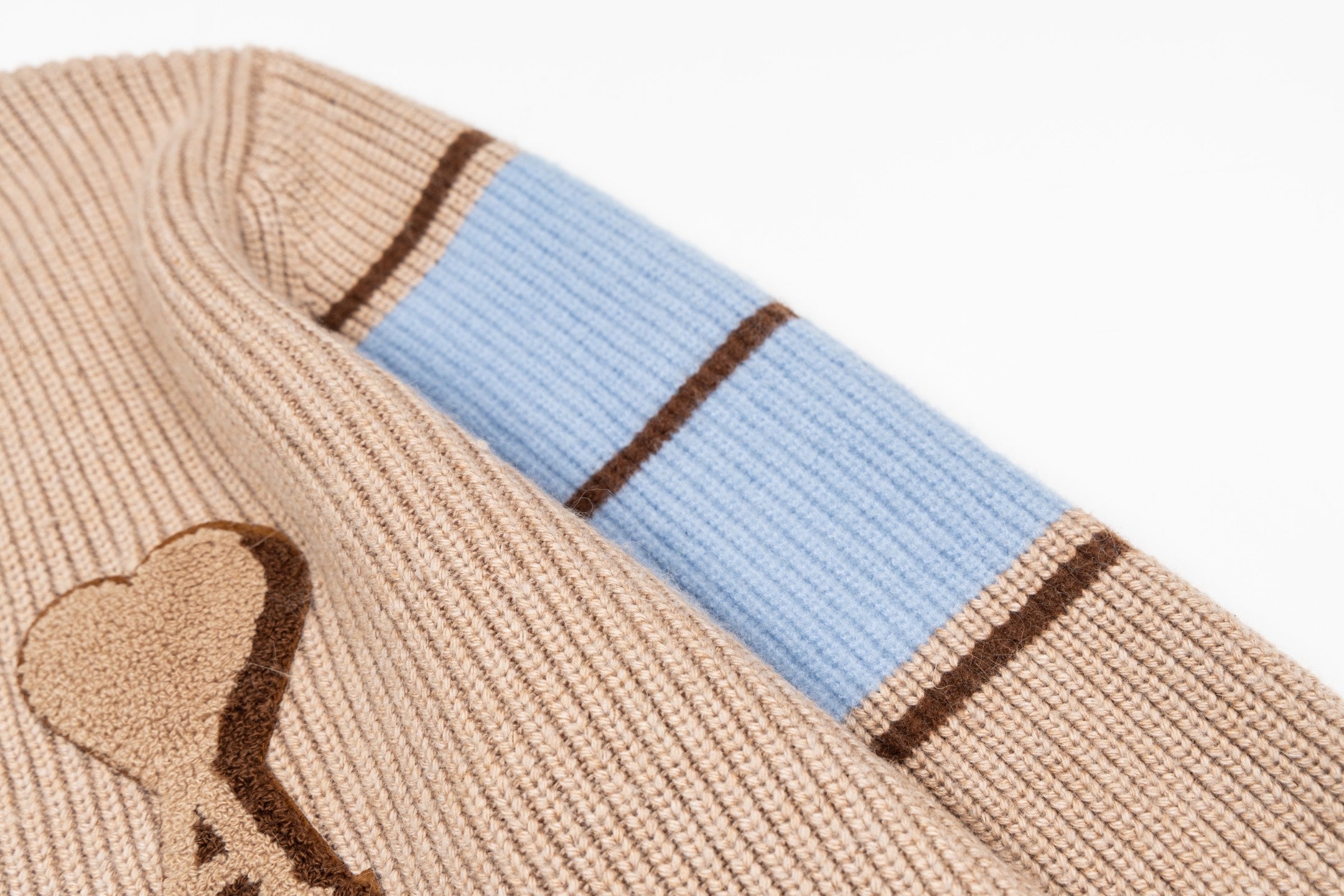 Beige knit sweater sleeve with blue cuff stripes and brown trim