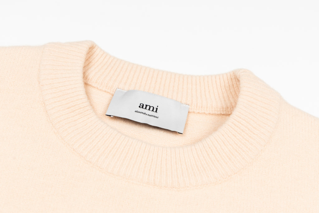 Light pink crewneck sweater neckline with ribbed collar and 'ami' label