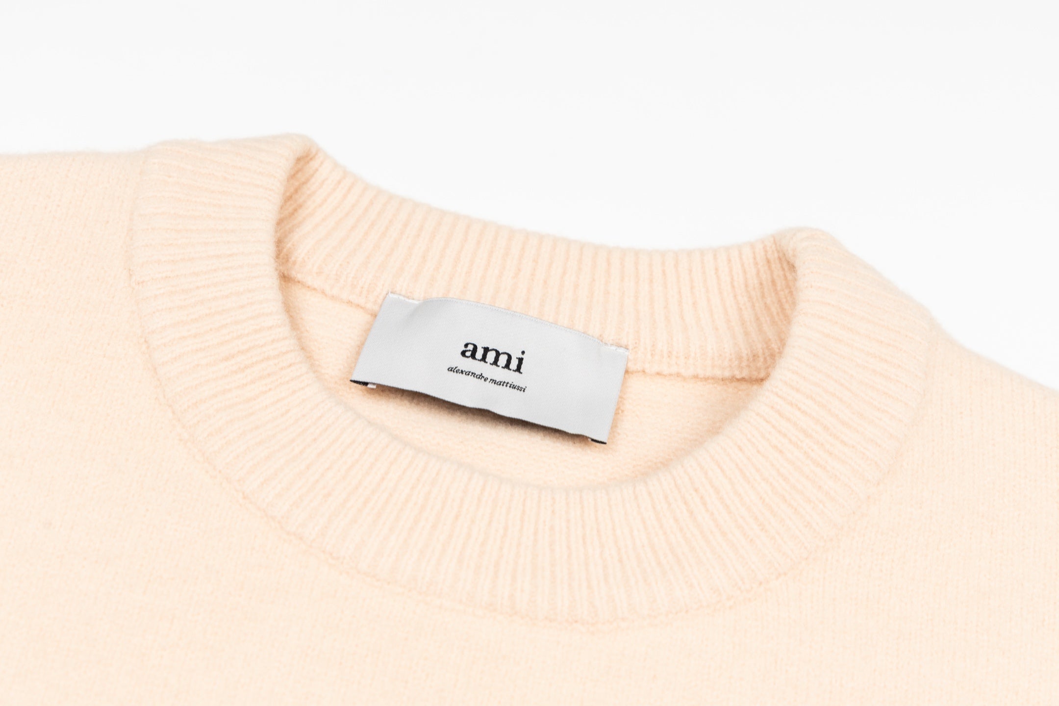 Light pink crewneck sweater neckline with ribbed collar and 'ami' label