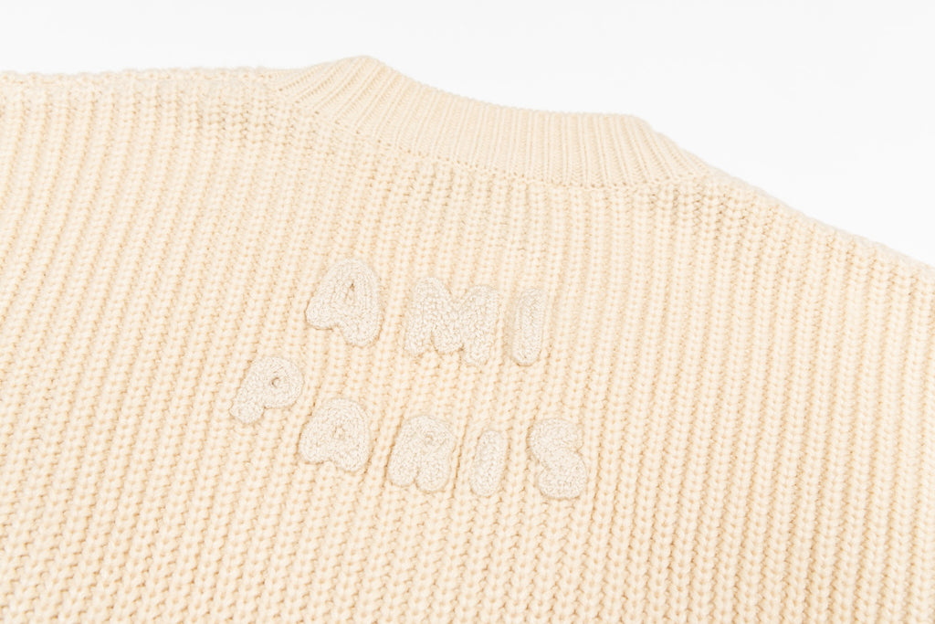 Cream knit sweater back with embossed script logo and ribbed striped hem