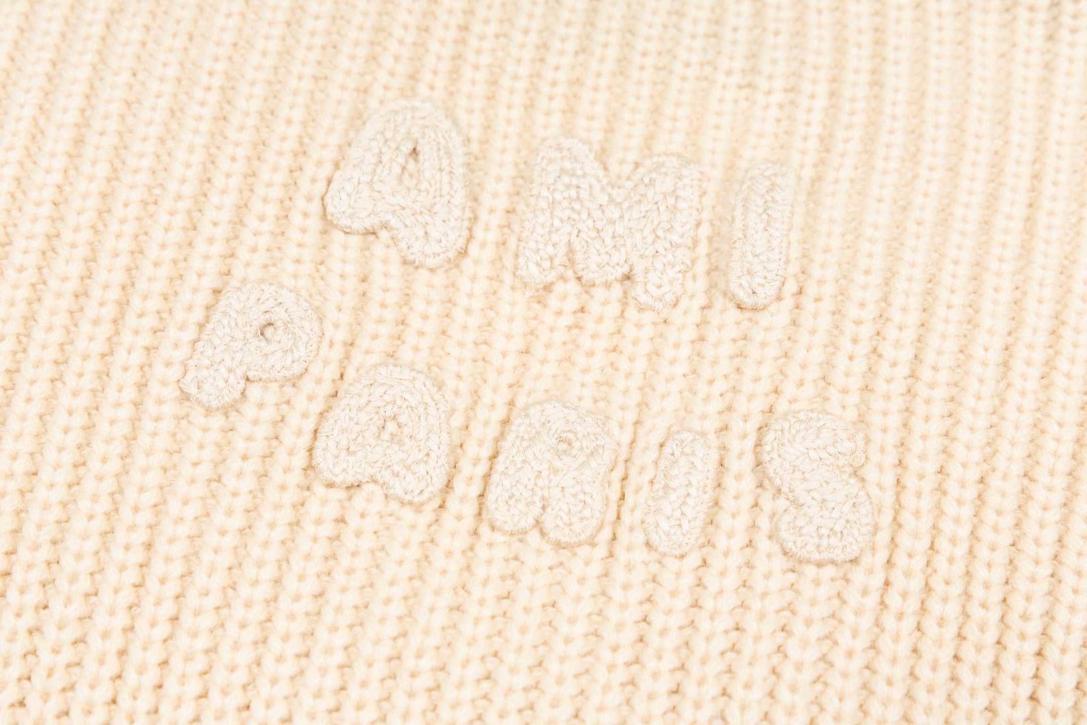 Cream knit sweater knit texture with raised embroidered script detail
