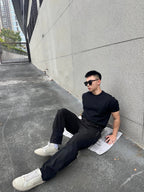 Black tapered pants in a seated pose with side pocket and cuffed hem