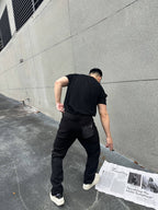 Back view of black tapered cargo-style pants with side pocket and cuffed hem