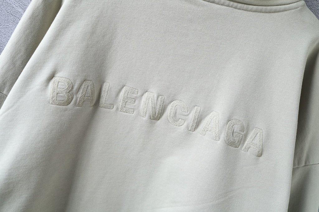 Close-up of embossed Balenciaga logo on the chest of an off-white hoodie