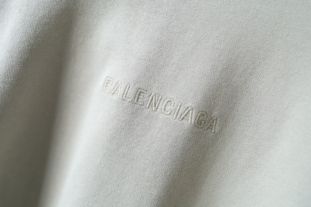 Close-up of embroidered Balenciaga logo on off-white hoodie fabric