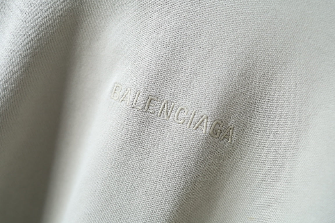 Close-up of embroidered Balenciaga logo on off-white hoodie fabric