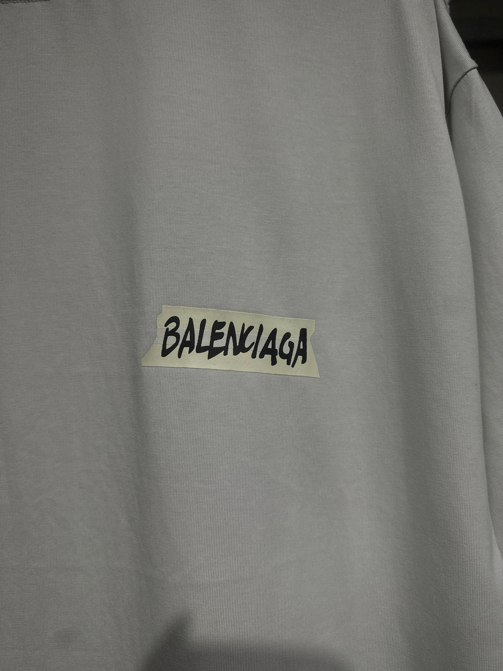 White Balenciaga T-shirt chest close-up with black logo text on yellow patch