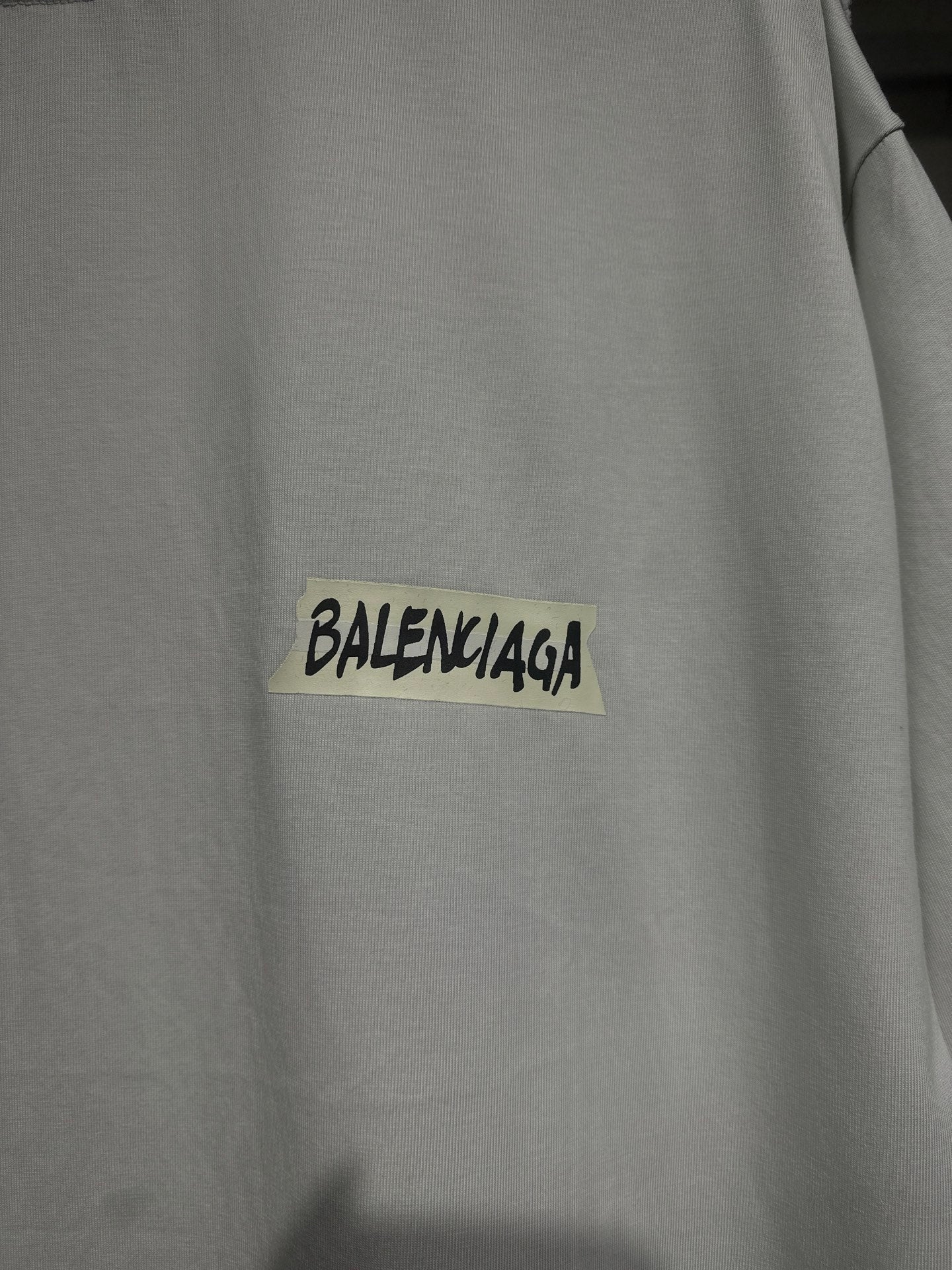 White Balenciaga T-shirt chest close-up with black logo text on yellow patch