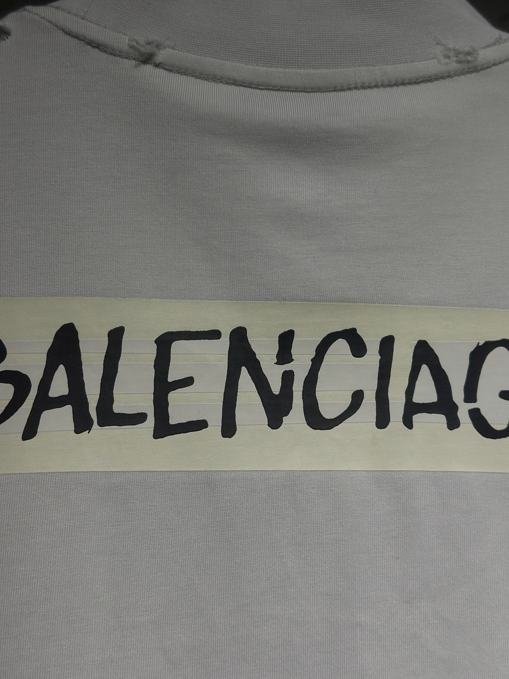 White Balenciaga T-shirt fabric close-up with black logo text on yellow patch
