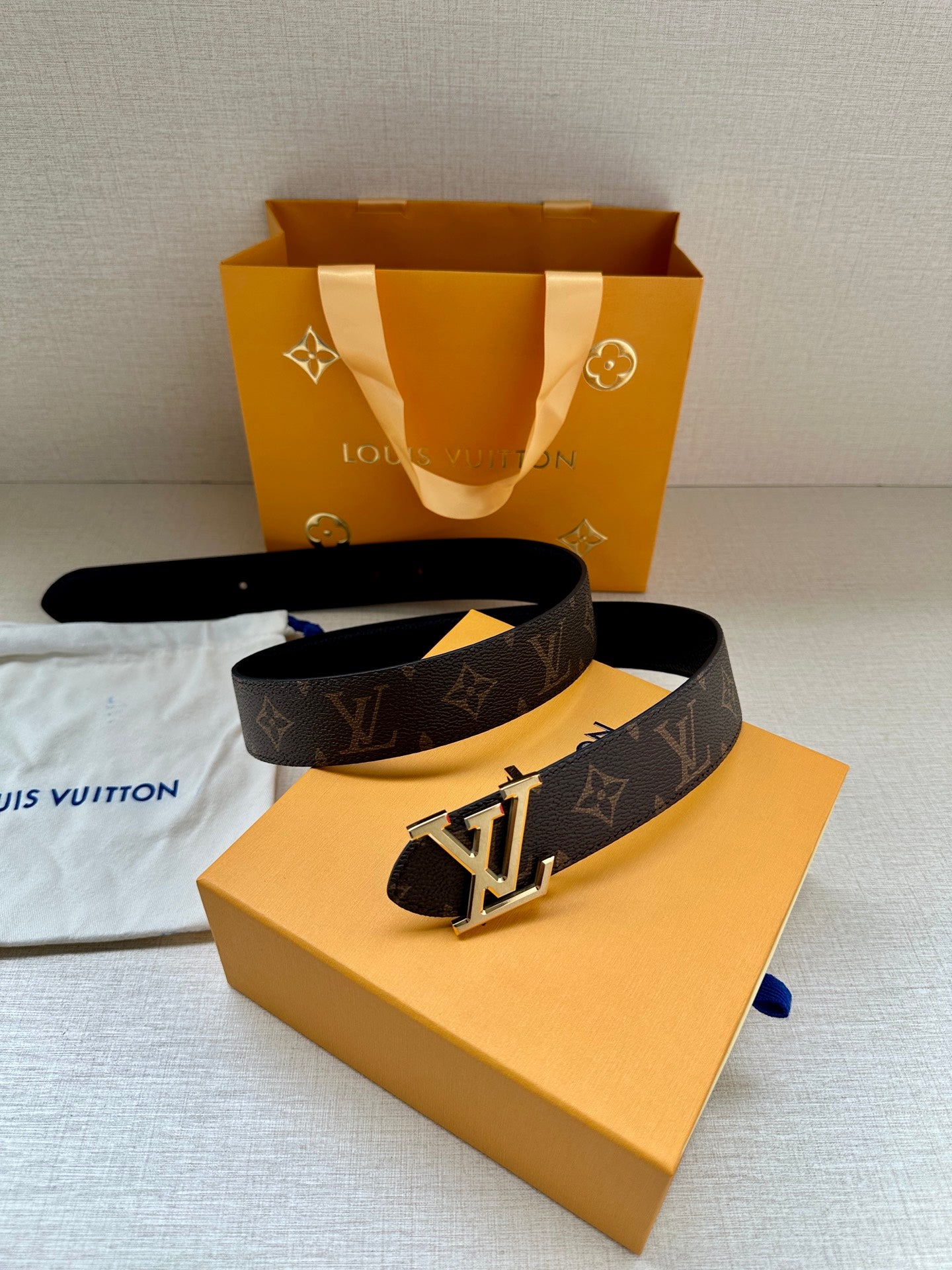 Dark monogram leather belt on orange box with silver-toned LV buckle.