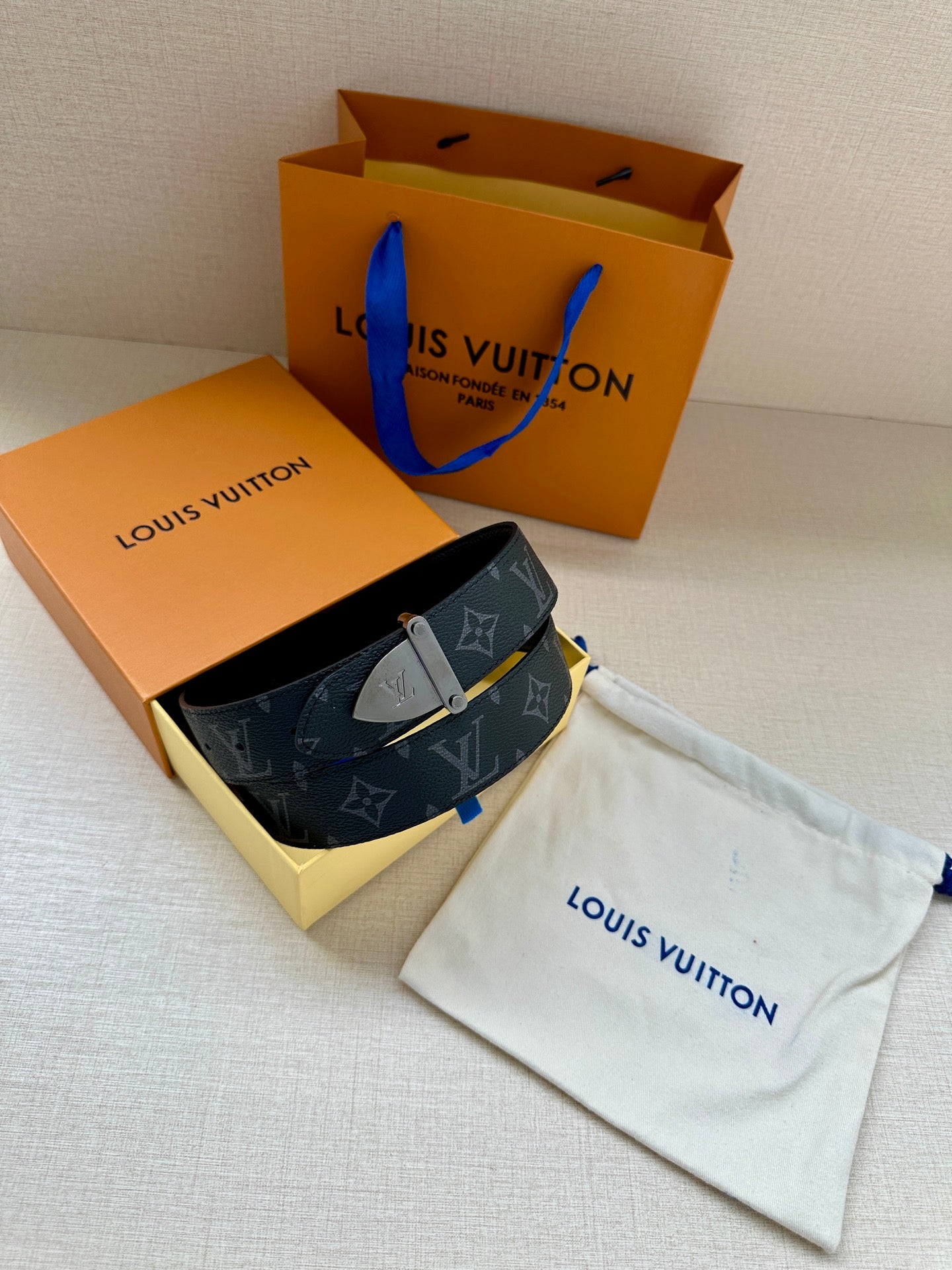 Monogram belt with dark strap and gold-tone clasp buckle on a storage pouch