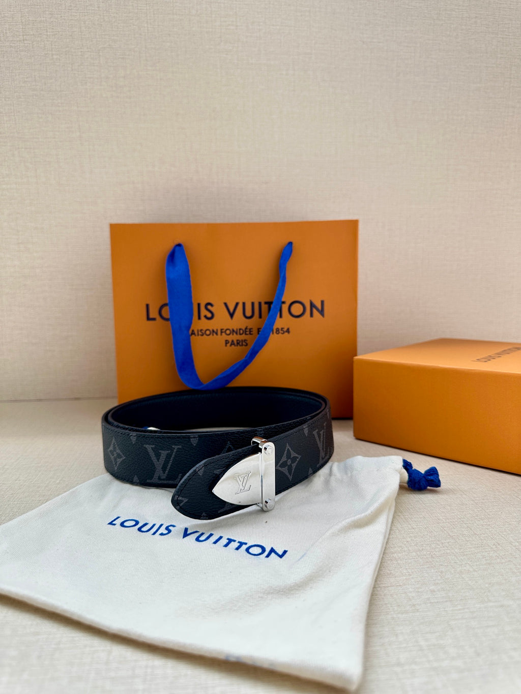 Monogram belt with dark strap and gold-tone clasp buckle beside storage pouch