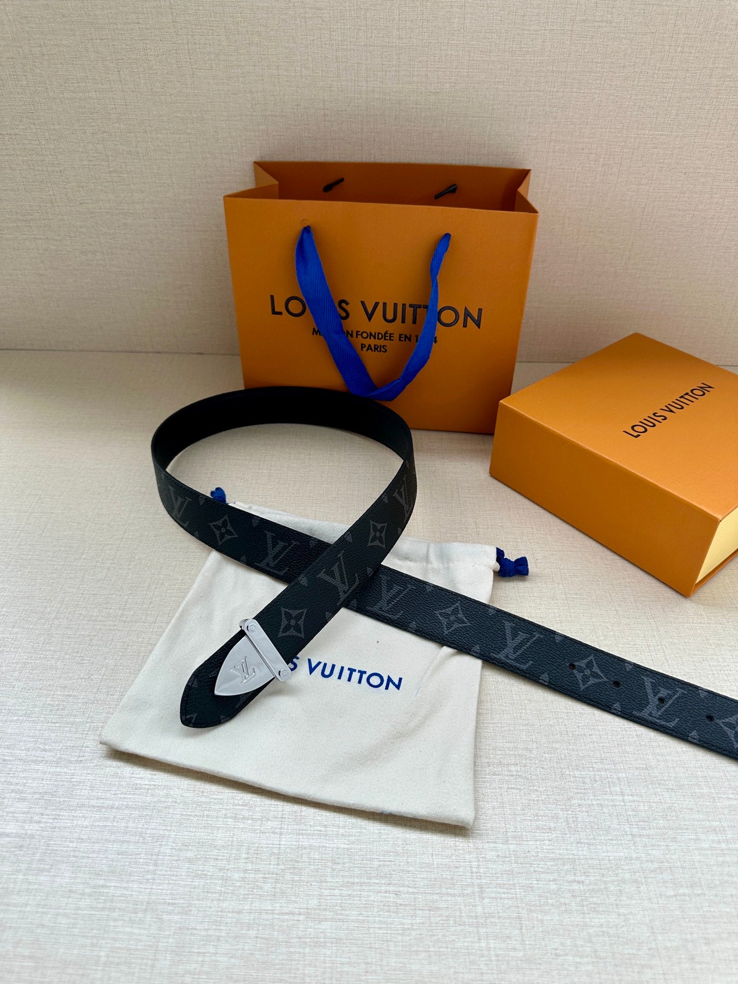Monogram belt with dark strap and gold-tone clasp buckle, laid out with pouch