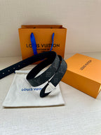 Monogram belt with dark strap and gold-tone clasp buckle, folded on a pouch