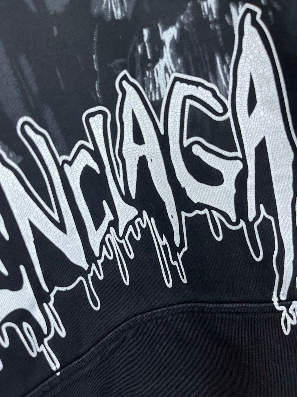 Dark hoodie with oversized white graffiti-style logo print on the chest.