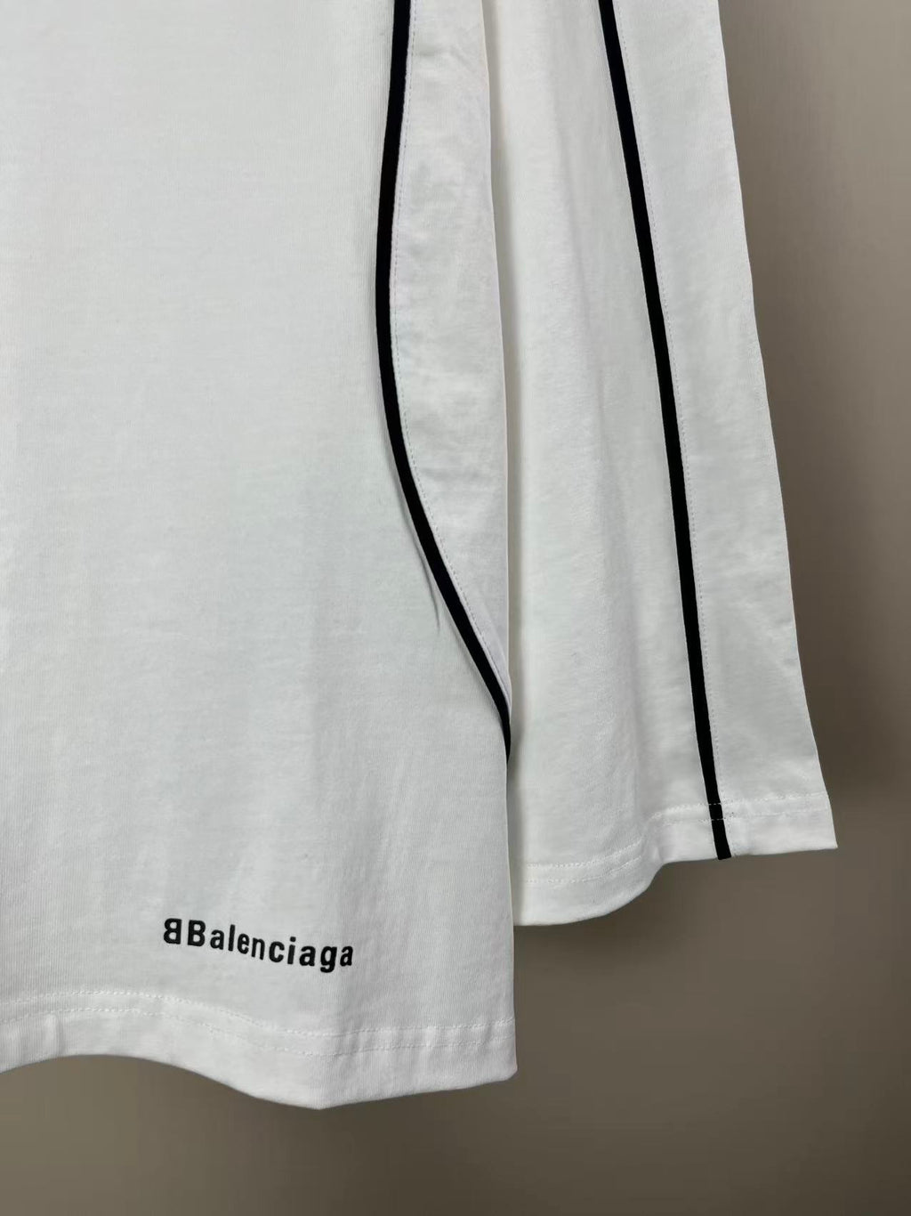 White jersey with short side slit, vertical black stripe, and small Balenciaga text
