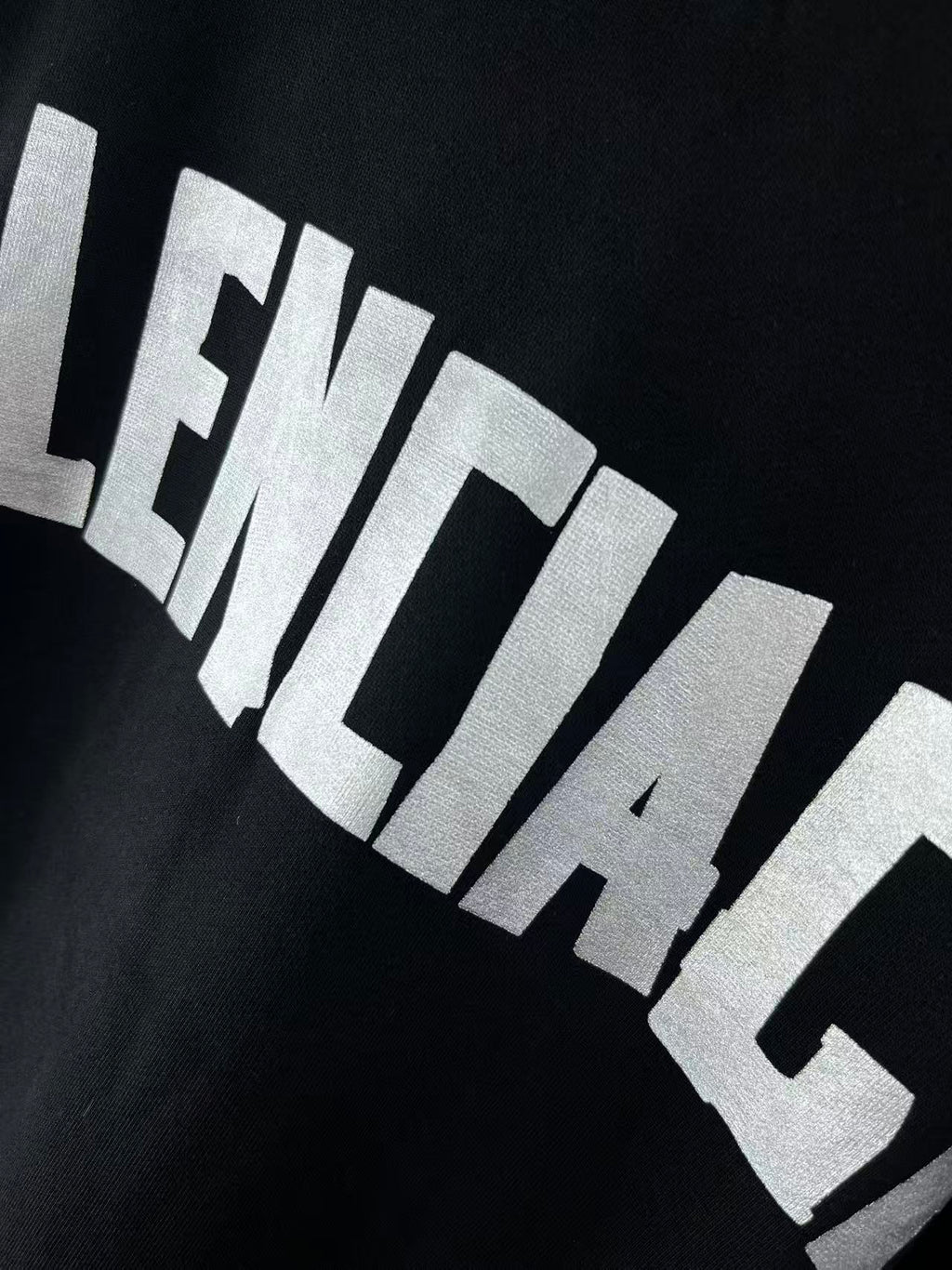 Close-up of white BALENCIAGA-style lettering across dark hoodie chest