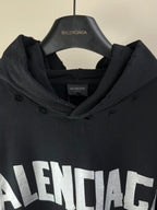 Long hoodie with black hood and front BALENCIAGA logo print, shown on hanger