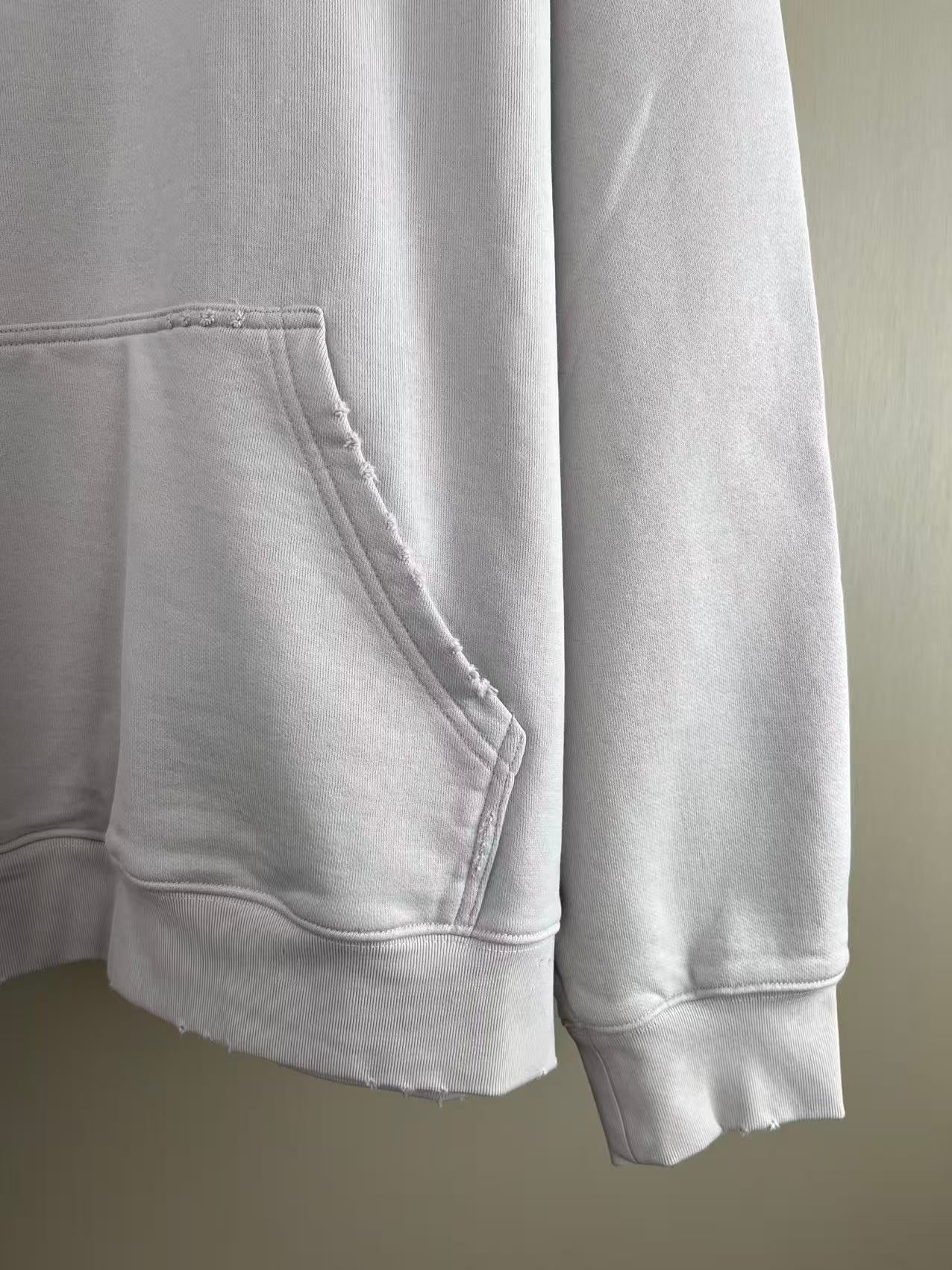 White hoodie pocket and hem close-up with stitched seams and ribbed cuffs