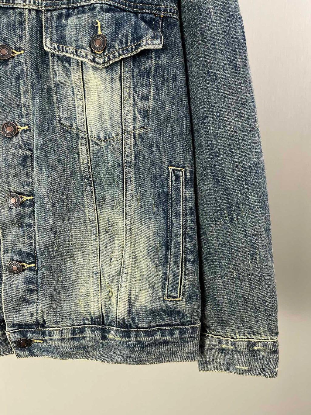 Washed blue denim jacket side seam and flap pockets with metal buttons