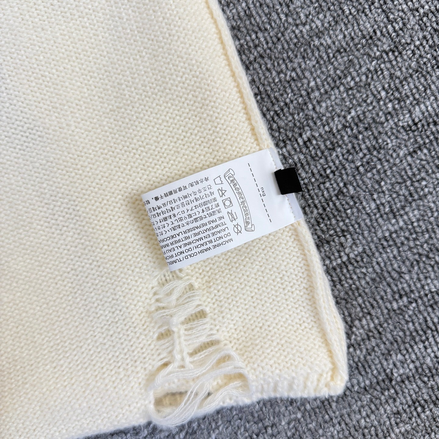 Cream knit sweater sleeve with size label and frayed embroidered trim