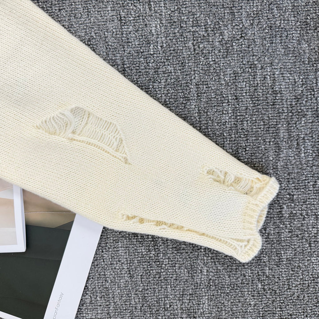 Cream knit sweater sleeve cuff with frayed embroidered edge