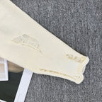 Cream knit sweater sleeve cuff with frayed embroidered edge
