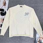 Cream knit sweater with blue floral-style emblem on front