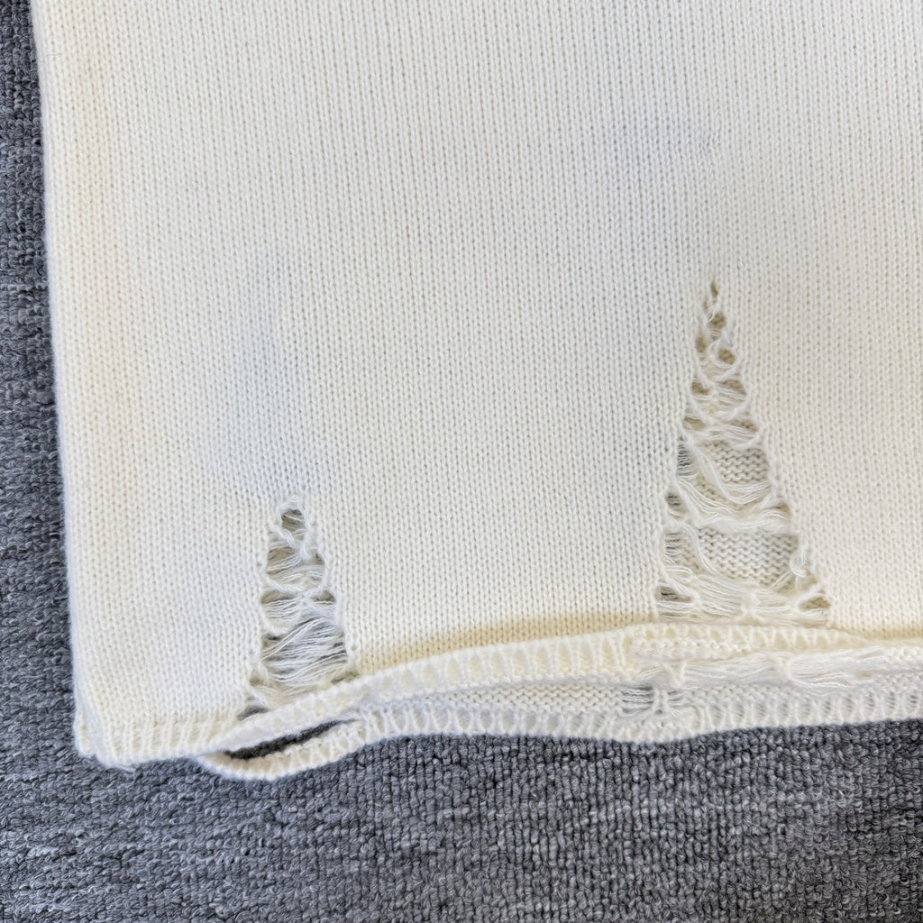 Cream knit sweater hem with frayed lace-like embroidery detail