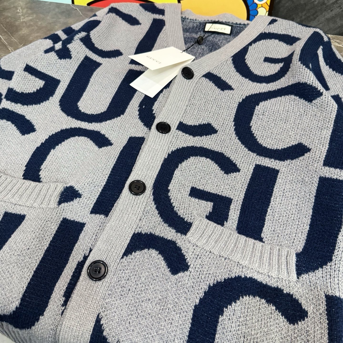Kids cardigan sweater close-up, light gray knit with navy Gucci-style logo pattern and buttons