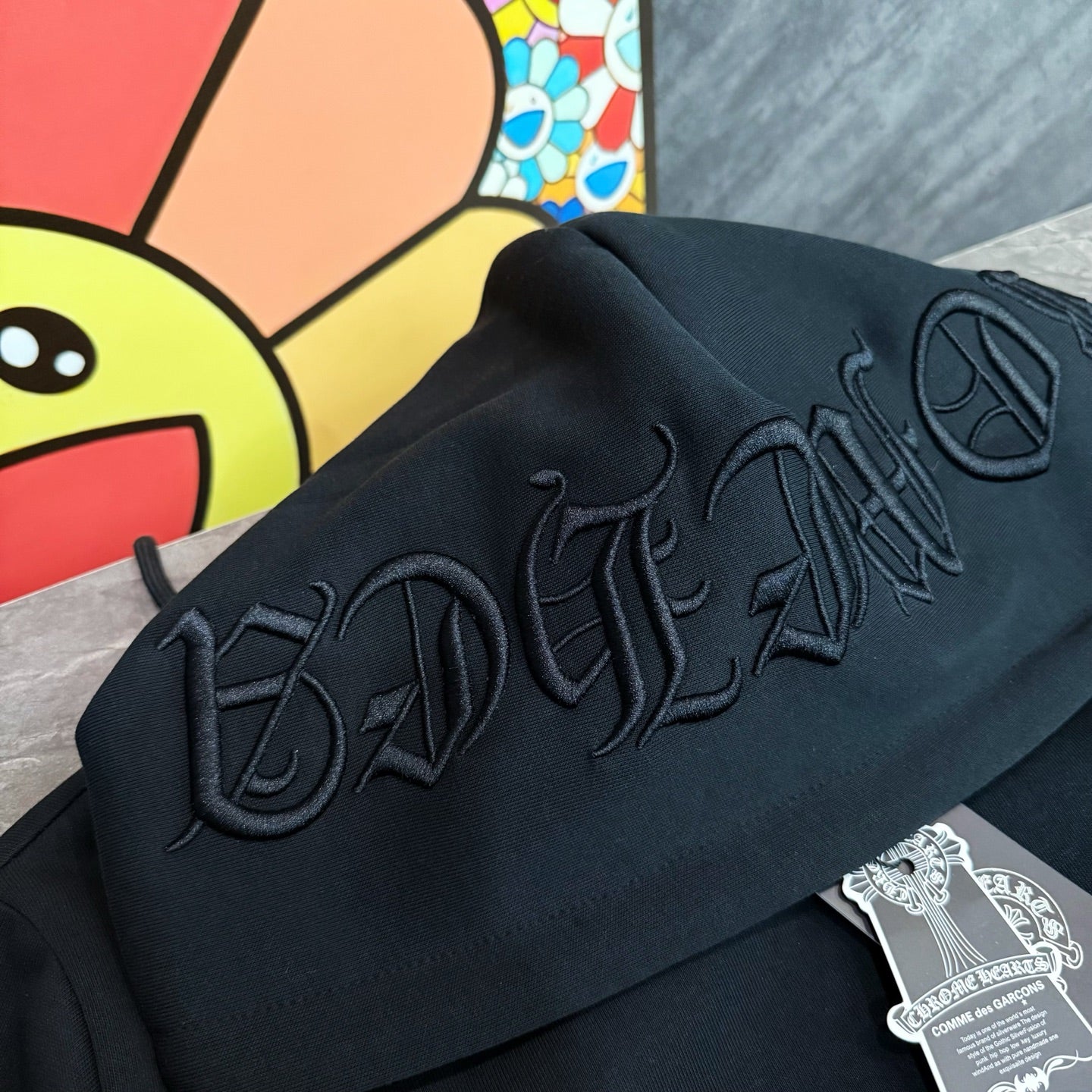 Black hoodie close-up of raised embroidered script on the hood and upper back