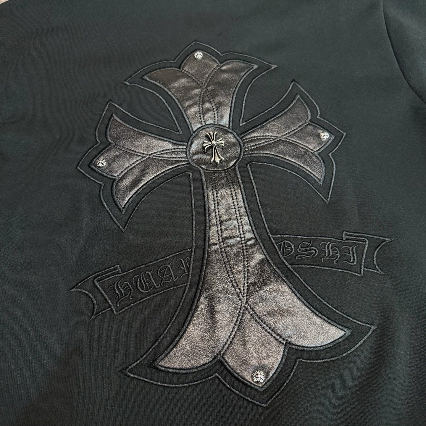Black hoodie close-up of large metallic bow-and-cross emblem