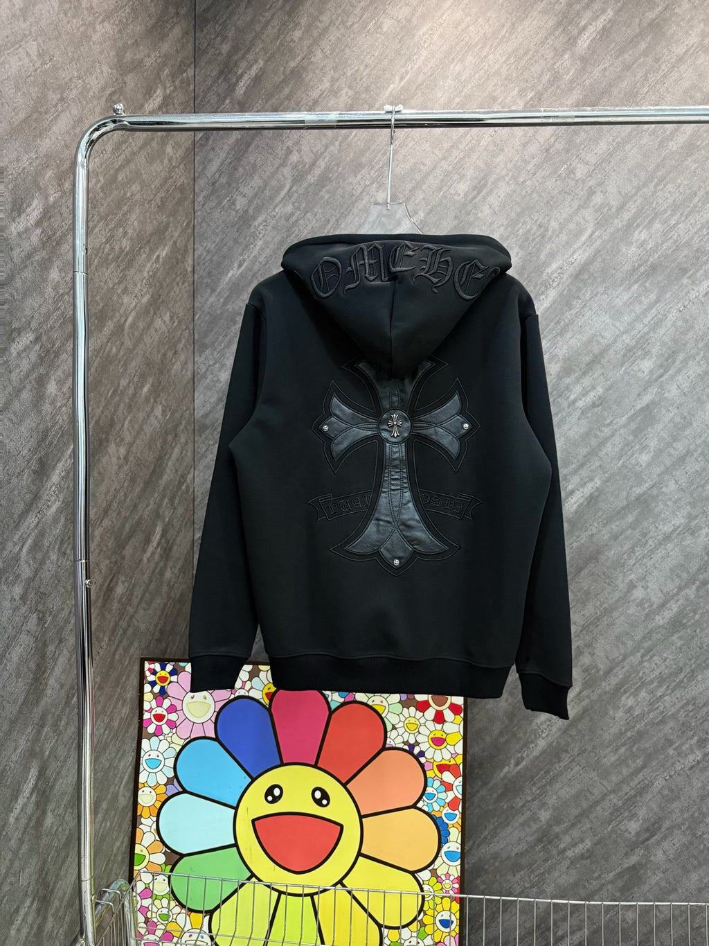 Black zip-up hoodie with hood and large bow-and-cross emblem on the back