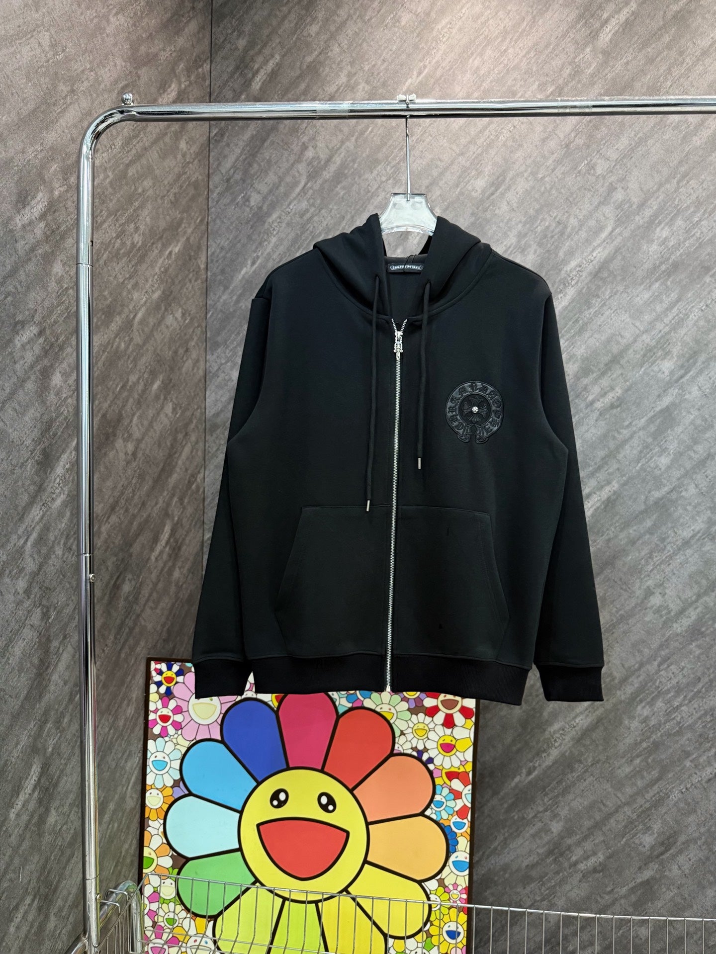 Black zip-up hoodie with hood and small circular emblem on the chest
