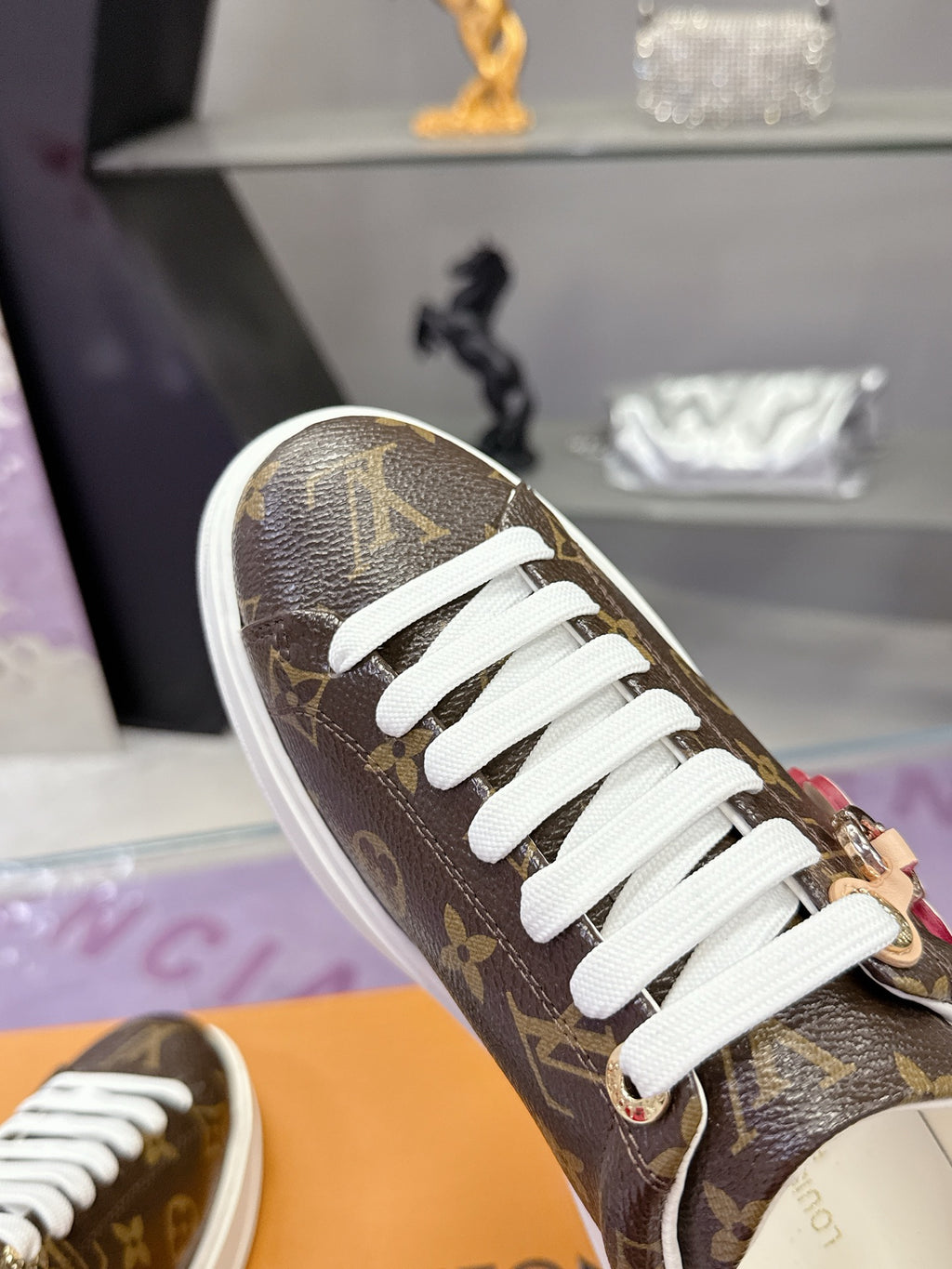 Louis Vuitton monogram sneaker close-up with white laces and metal charm.