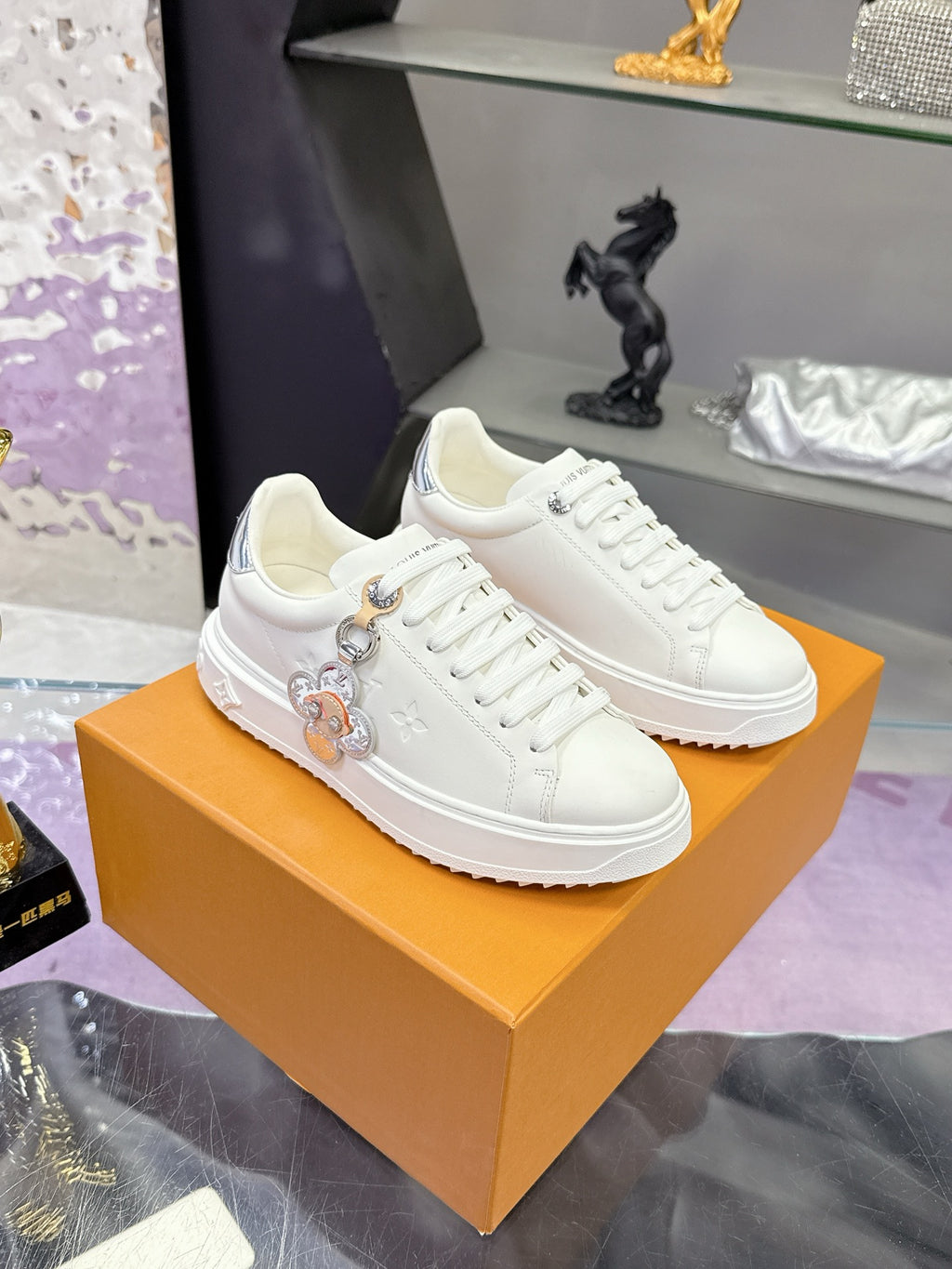 White Louis Vuitton sneakers on an orange box; lace-up style with charm hardware