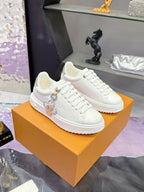White Louis Vuitton sneakers on an orange box; lace-up style with charm hardware